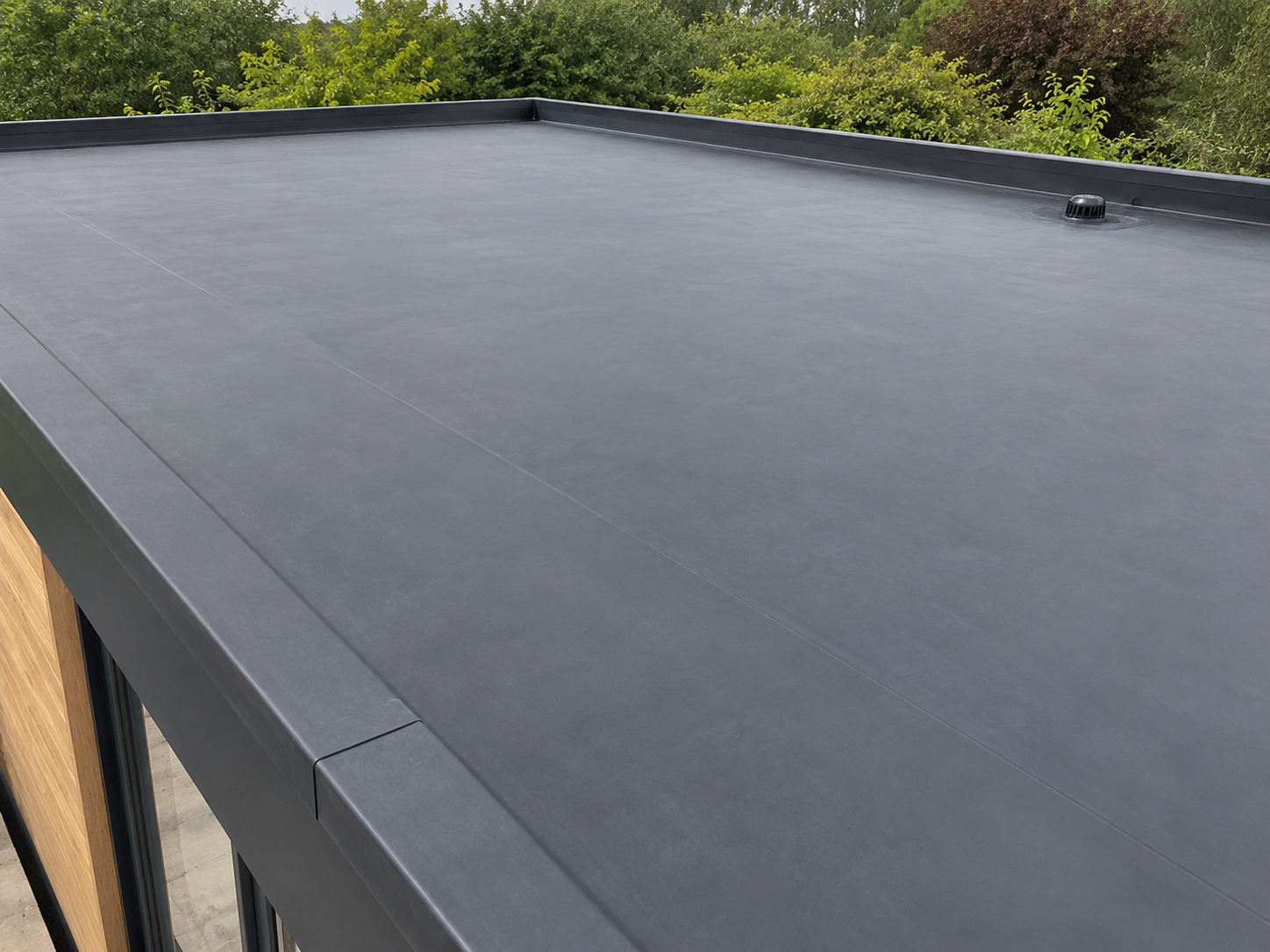 Completed dark grey EPDM flat roof surrounded by greenery